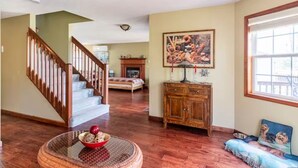 Un ampio soggiorno con parquet, una scala in legno, un caminetto e un grande quadro appeso al muro.