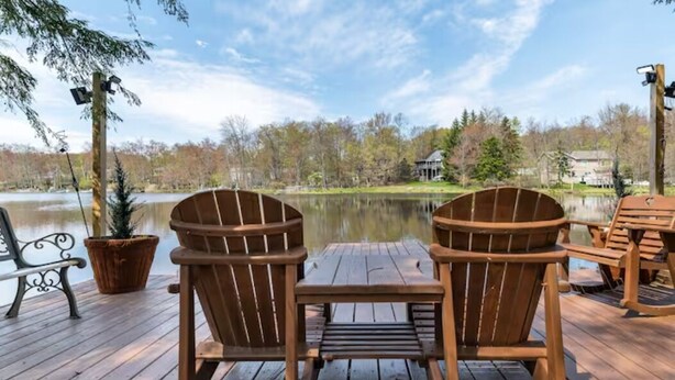 Un pontile in legno con due poltrone Adirondack rivolte verso un lago, un tavolino e una pianta in vaso.