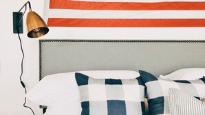 Una cama con almohadas a cuadros, una lámpara de pared y una bandera estadounidense.