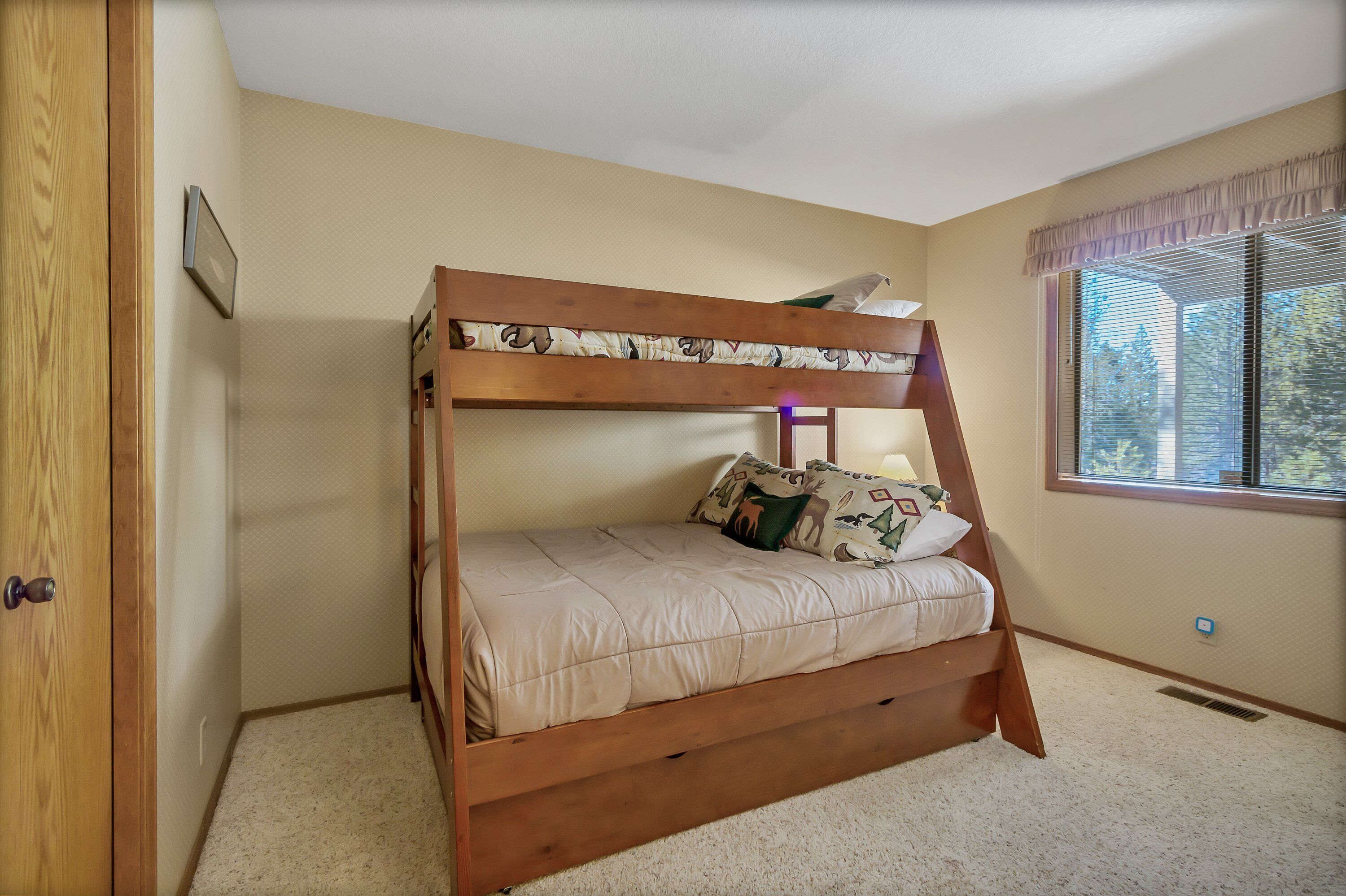 A bunk bed with a wooden frame and beige bedding, a window with blinds, and a door with a wooden frame.