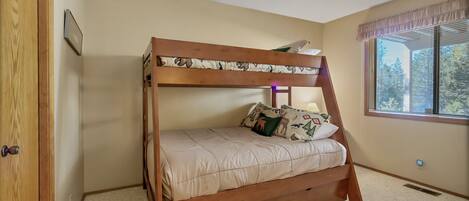 A bunk bed with a wooden frame and beige bedding, a window with blinds, and a door with a wooden frame.