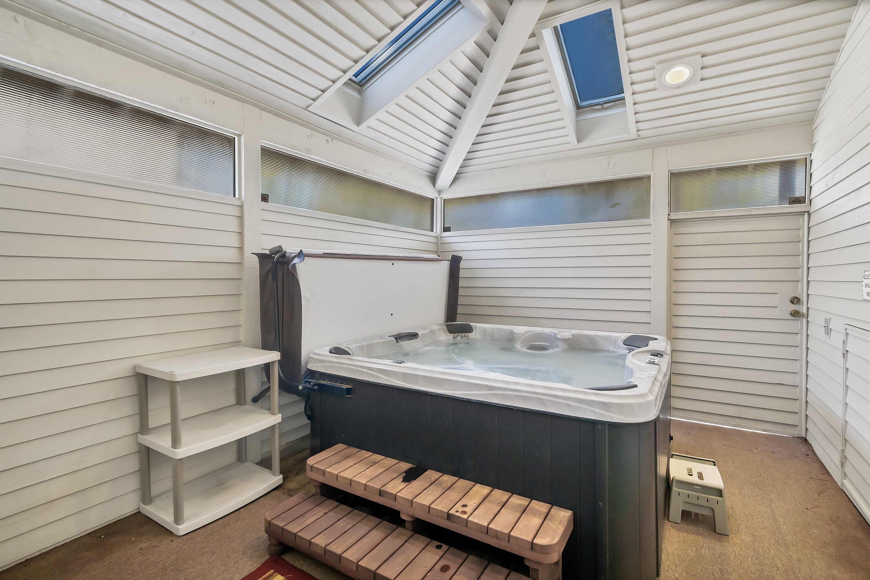 A hot tub in a corner of a room with a sloped ceiling, wooden benches, and a small step stool.