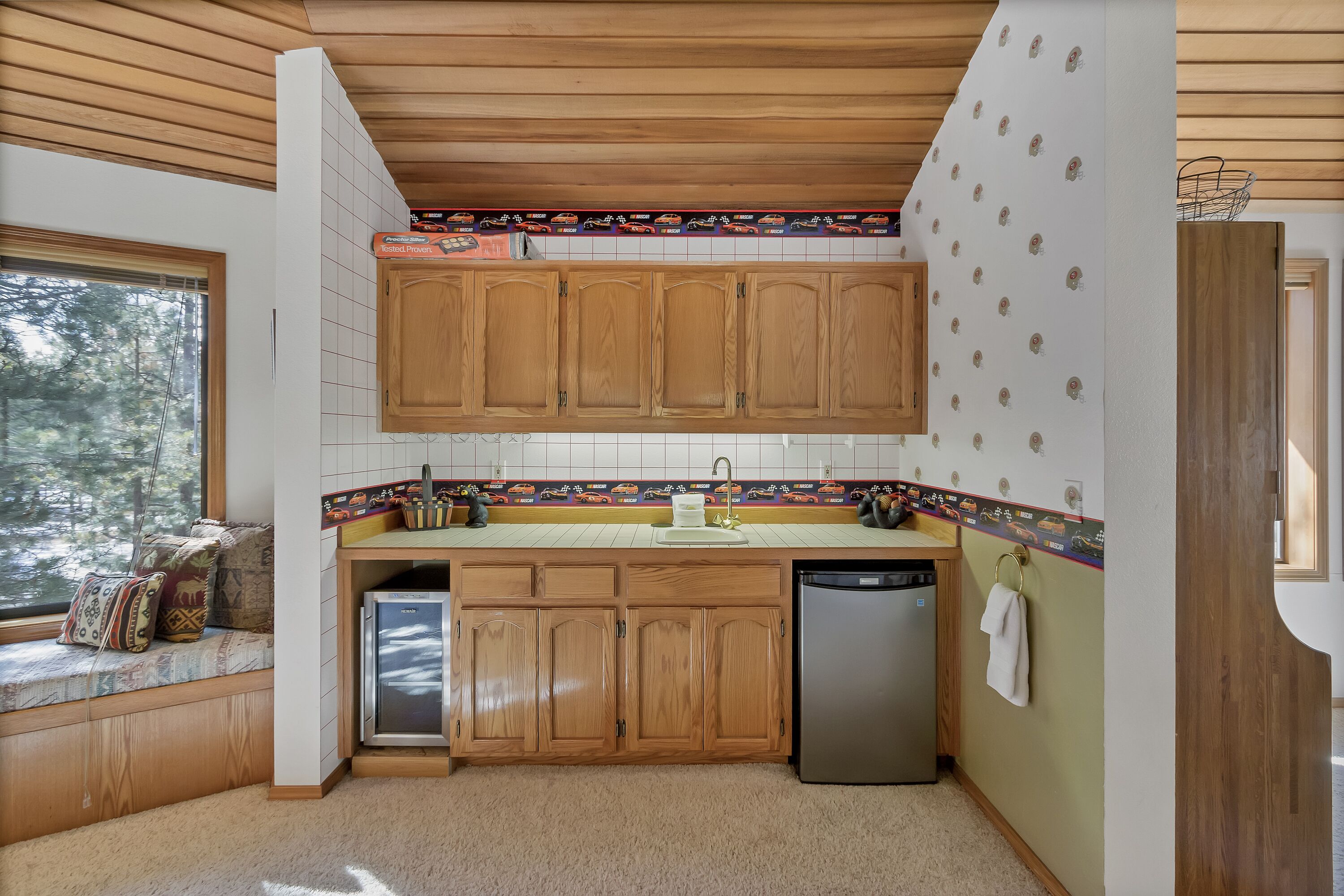 Una cucina con mobili in legno, lavastoviglie integrata e una panca finestrella con cuscini.