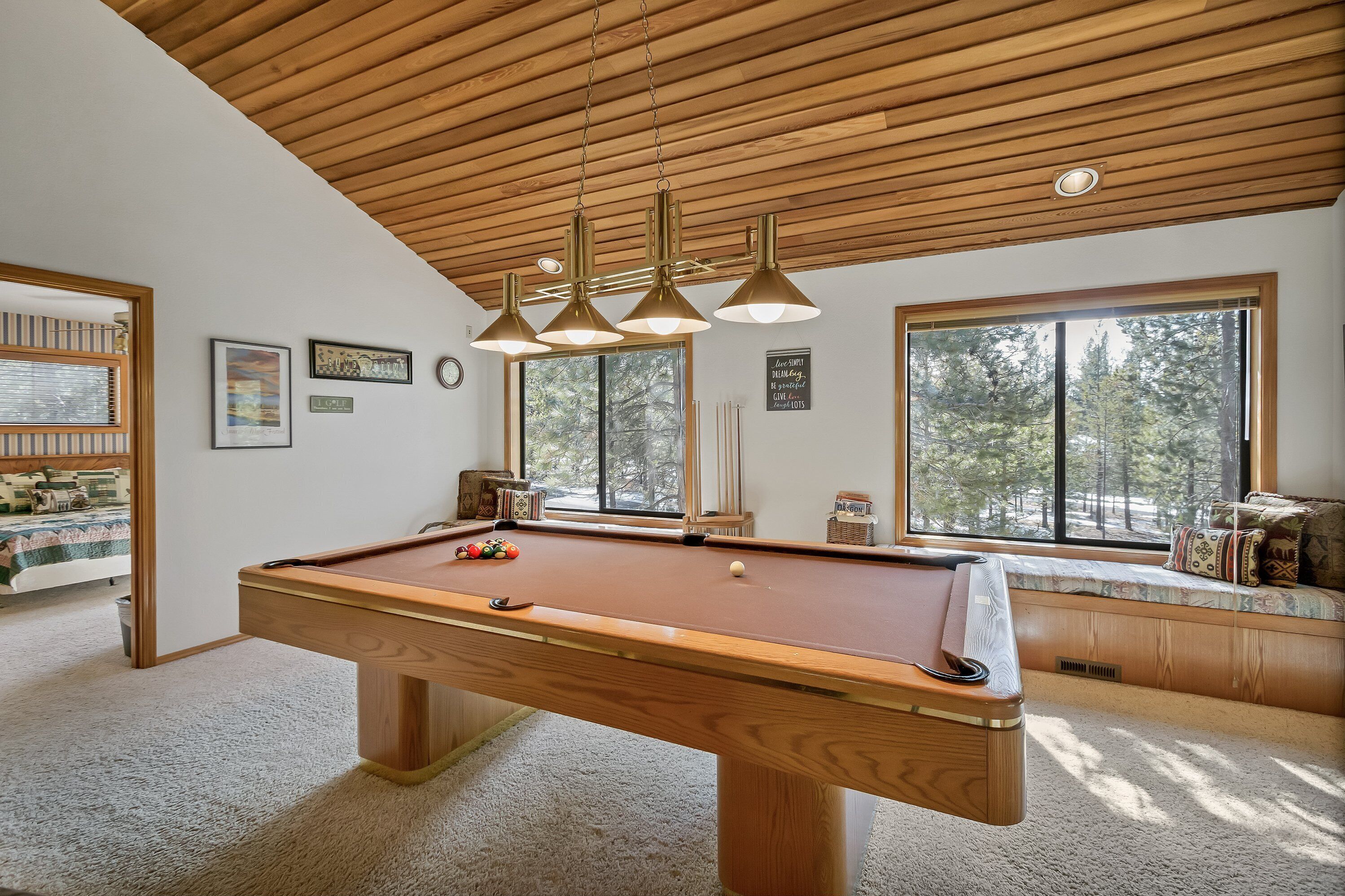 A pool table in a room with wooden ceiling beams, large windows, and a view of trees.