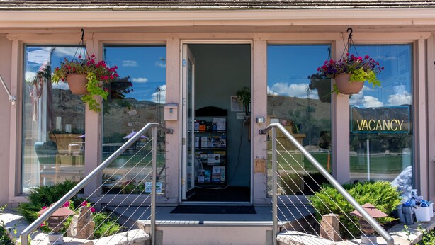 Entrada de hotel con un cartel de 'VACANCY', una escalera y cestas de flores colgantes.