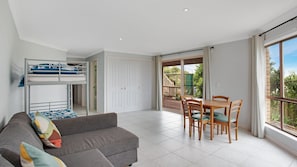 Une pièce moderne et bien éclairée, équipée d’un lit superposé, d’un canapé, d’une table à manger avec des chaises et de grandes fenêtres donnant sur un paysage verdoyant.