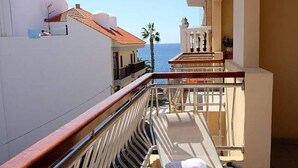 Varanda com vista para o mar, uma palmeira e um edifício com telhado de azulejos.
