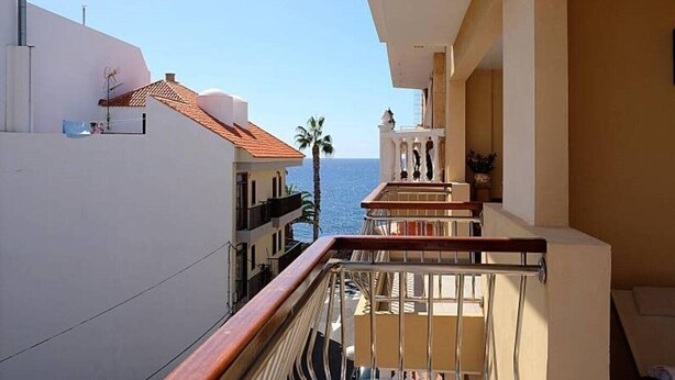 Varanda com vista para o mar, uma palmeira e um edifício com telhado de azulejos.