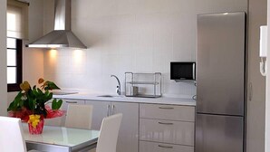 Cozinha moderna com geladeira de aço inoxidável, micro-ondas e pia. Há uma mesa de jantar com cadeiras e um vaso de planta.