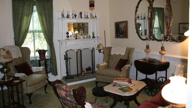 A traditional living room with a fireplace, two armchairs, a coffee table, and a large ornate mirror. - Country Manor - Lower floor (Henderson)