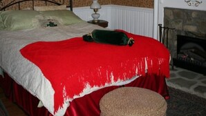 A room with a bed, a red and white bedspread, a chandelier, a fireplace, and a patterned carpet. - Country Manor - Lower floor (Henderson)