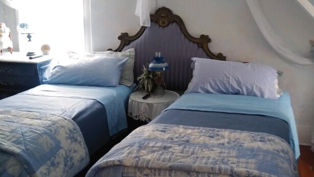 A bedroom with two beds, a nightstand, a lamp, and a decorative item on the nightstand. - Country Manor - Top Floor (Henderson)