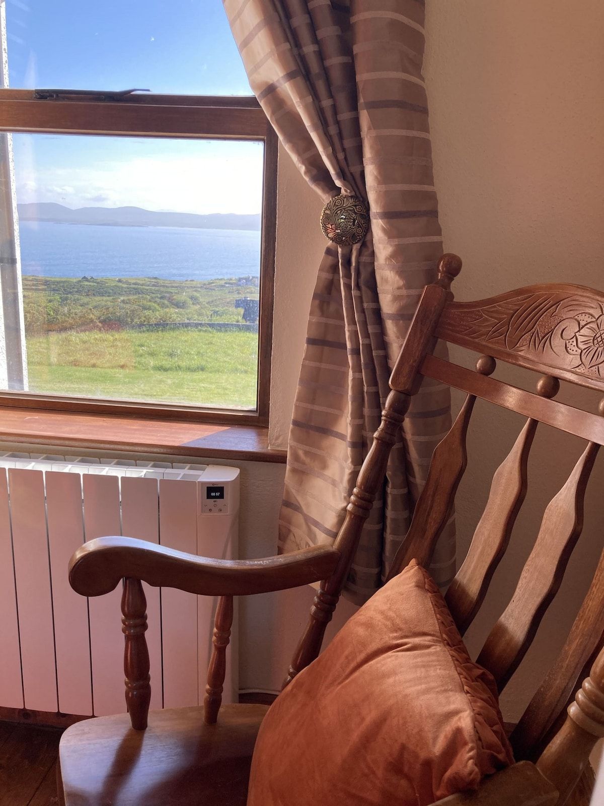 A wooden chair with a cushion, positioned near a window with a view of a landscape.