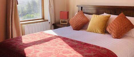 A bedroom with a bed, a nightstand, a mirror, and a window with curtains.