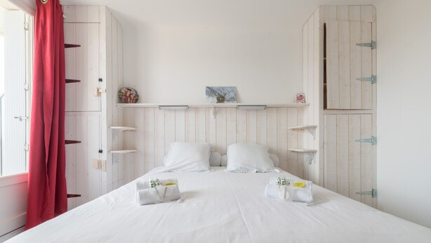 A bedroom with a bed, white curtains, and wooden cabinets. - L'Amiral - Plage - Parking (La Bernerie-en-Retz)