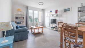 A spacious living area with a sofa, a dining table with chairs, a TV, and a bookshelf. - L'Amiral - Plage - Parking (La Bernerie-en-Retz)