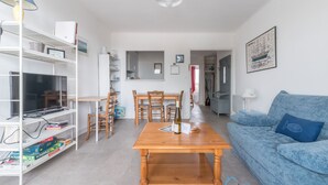 A living room with a wooden table, blue sofa, and a TV on a shelf. - L'Amiral - Plage - Parking (La Bernerie-en-Retz)