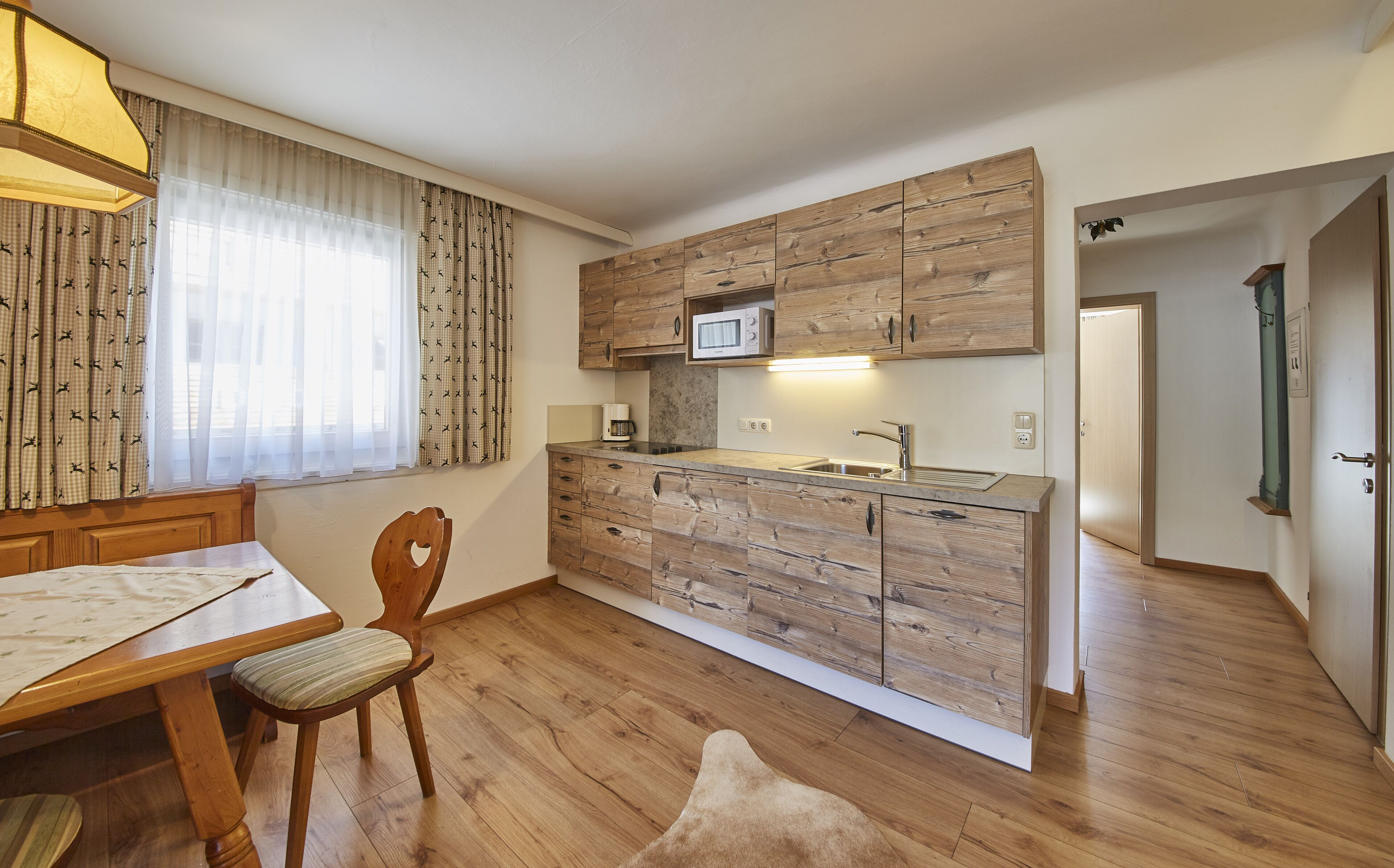 A compact kitchen with wooden cabinetry, a microwave, and a dining area with a table and chairs.