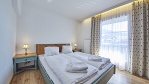 A bedroom with a double bed, two bedside tables with lamps, a view of a cityscape through large windows, and a patterned curtain. - TownHouse Appartements (Saalbach-Hinterglemm)
