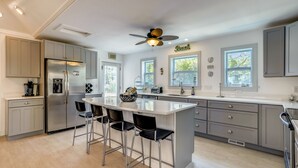 Une cuisine moderne dotée d’un îlot central, de tabourets de bar, d’un réfrigérateur et d’un ventilateur de plafond.