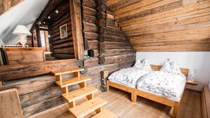 Ein Schlafzimmer in einer Blockhütte mit einem hölzernen Bett, einem kleinen Tisch und einer Treppe.