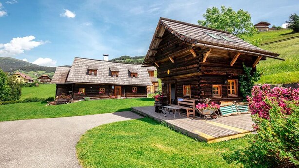 Eine rustikale Holzhütte mit Veranda, umgeben von üppigem Grün und blauem Himmel.