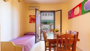 A compact room with a bed, a dining table with chairs, a sliding glass door leading to a balcony, and a wall-mounted air conditioner. - 1990 Appartamento Azzurra (Gallipoli)