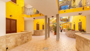 A bright yellow interior with stone columns, wooden shutters, and a tiled floor. - 1990 Appartamento Azzurra (Gallipoli)