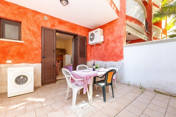 A small patio with a washing machine, a table with chairs, and a door leading to an interior space.