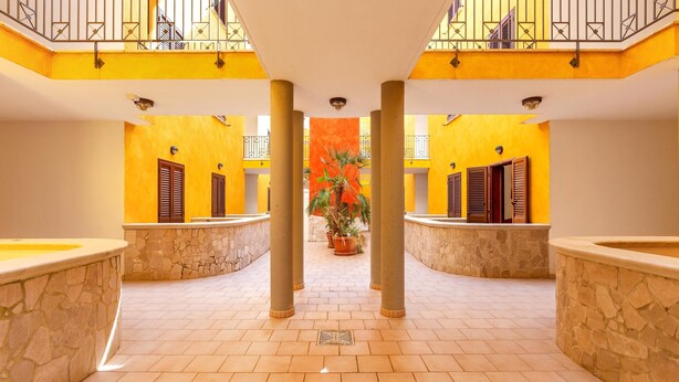 A spacious atrium with a tiled floor, stone columns, and a central potted plant. - 1990 Appartamento Azzurra (Gallipoli)