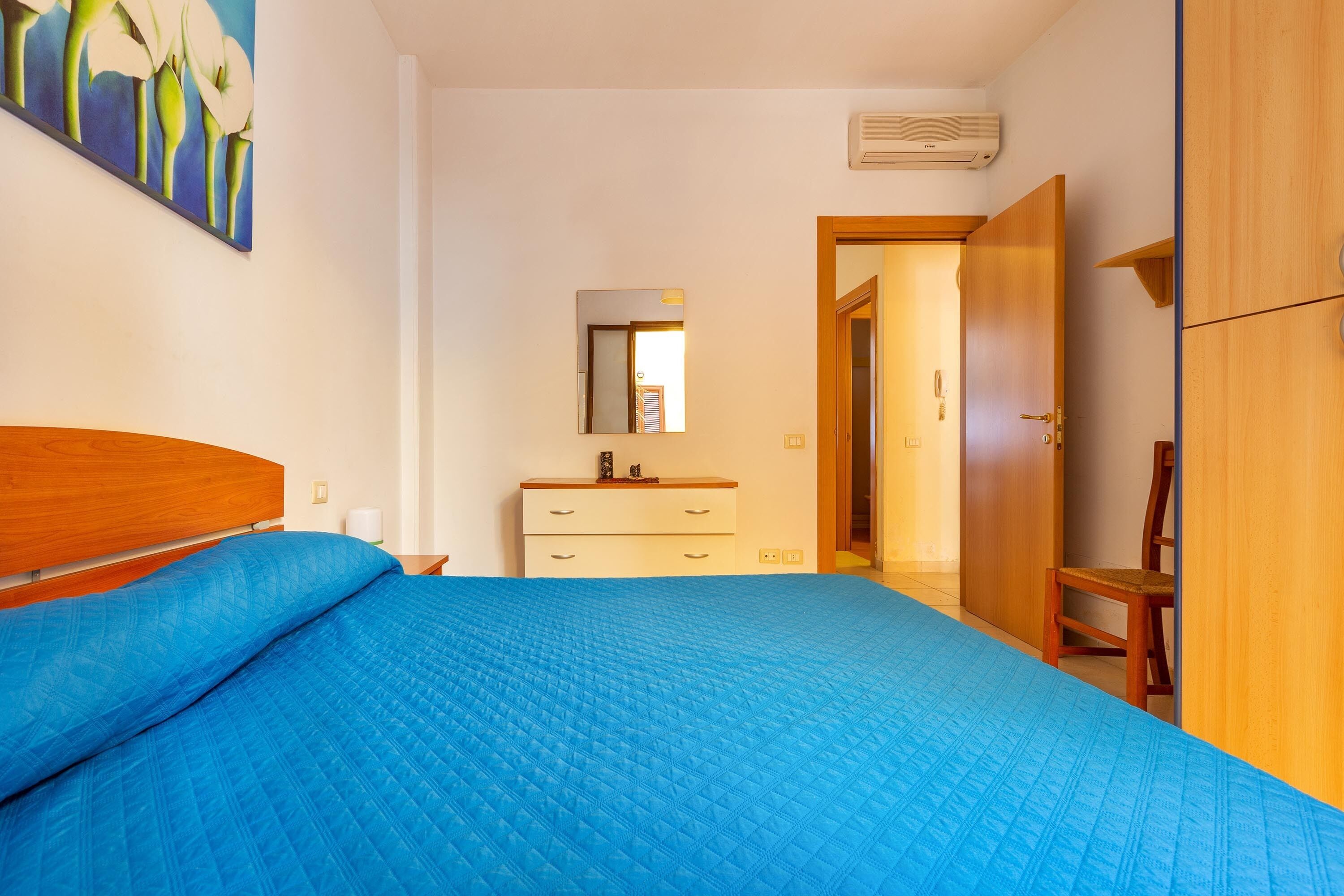 A bedroom with a bed, a dresser, a mirror, and a door leading to another room.