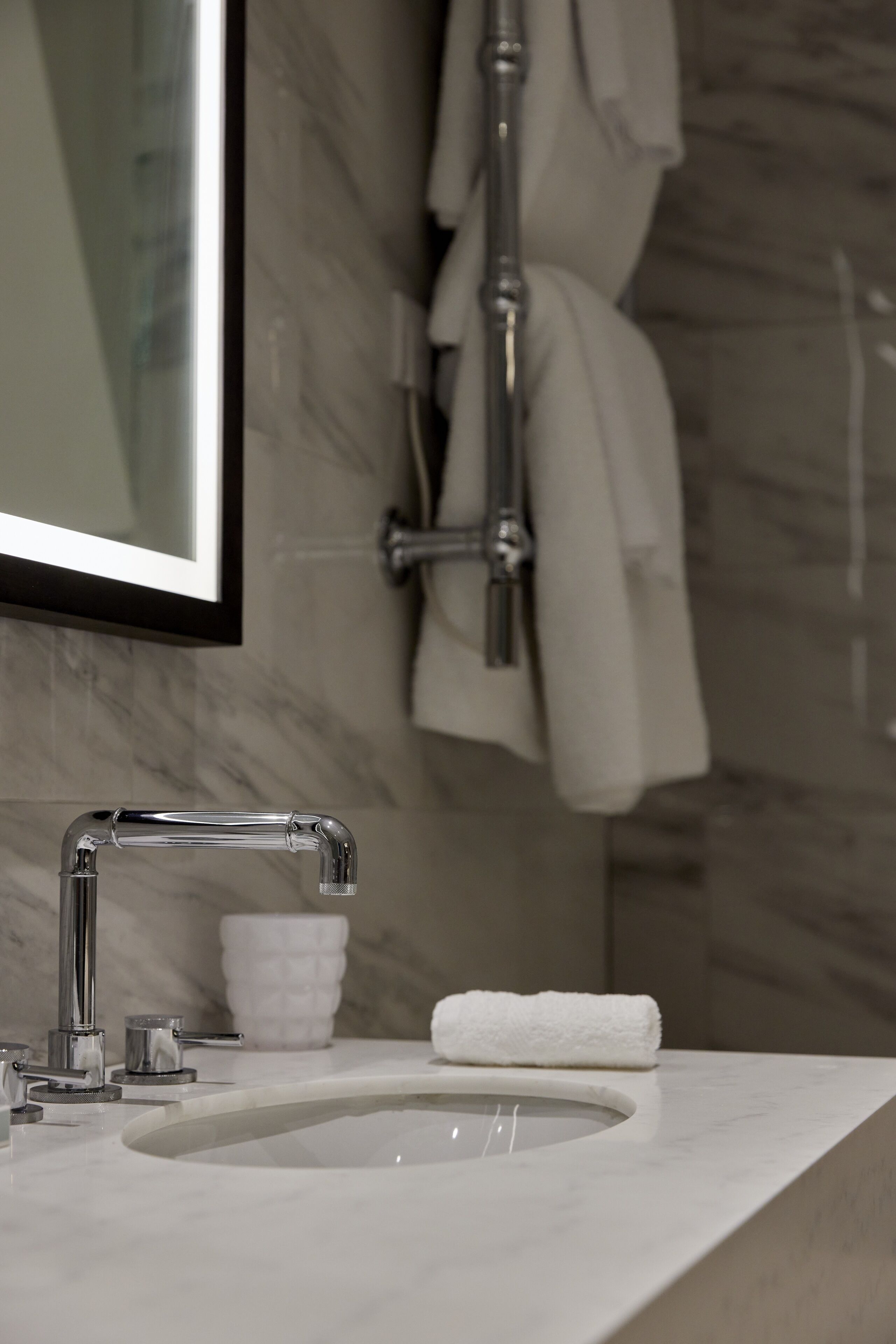 A bathroom with a marble sink, a mirror, and a towel rack.