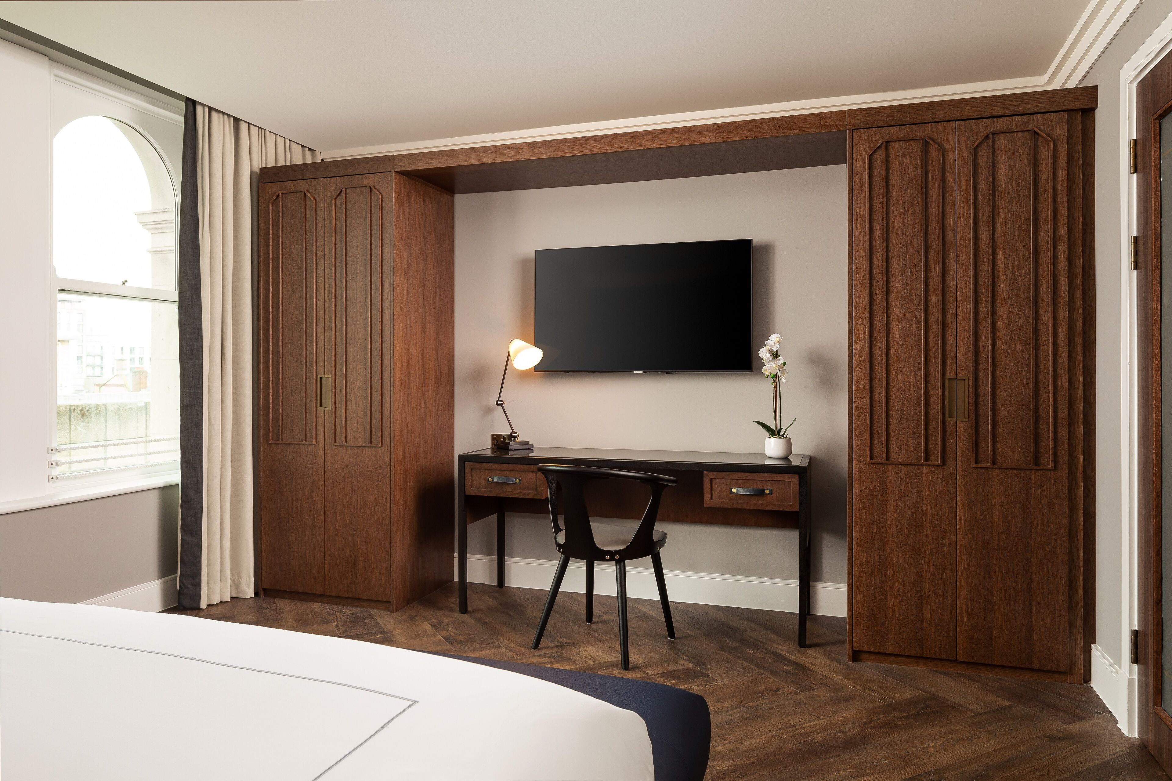 A bedroom with a bed, a desk, a chair, a TV, and wooden wardrobes.