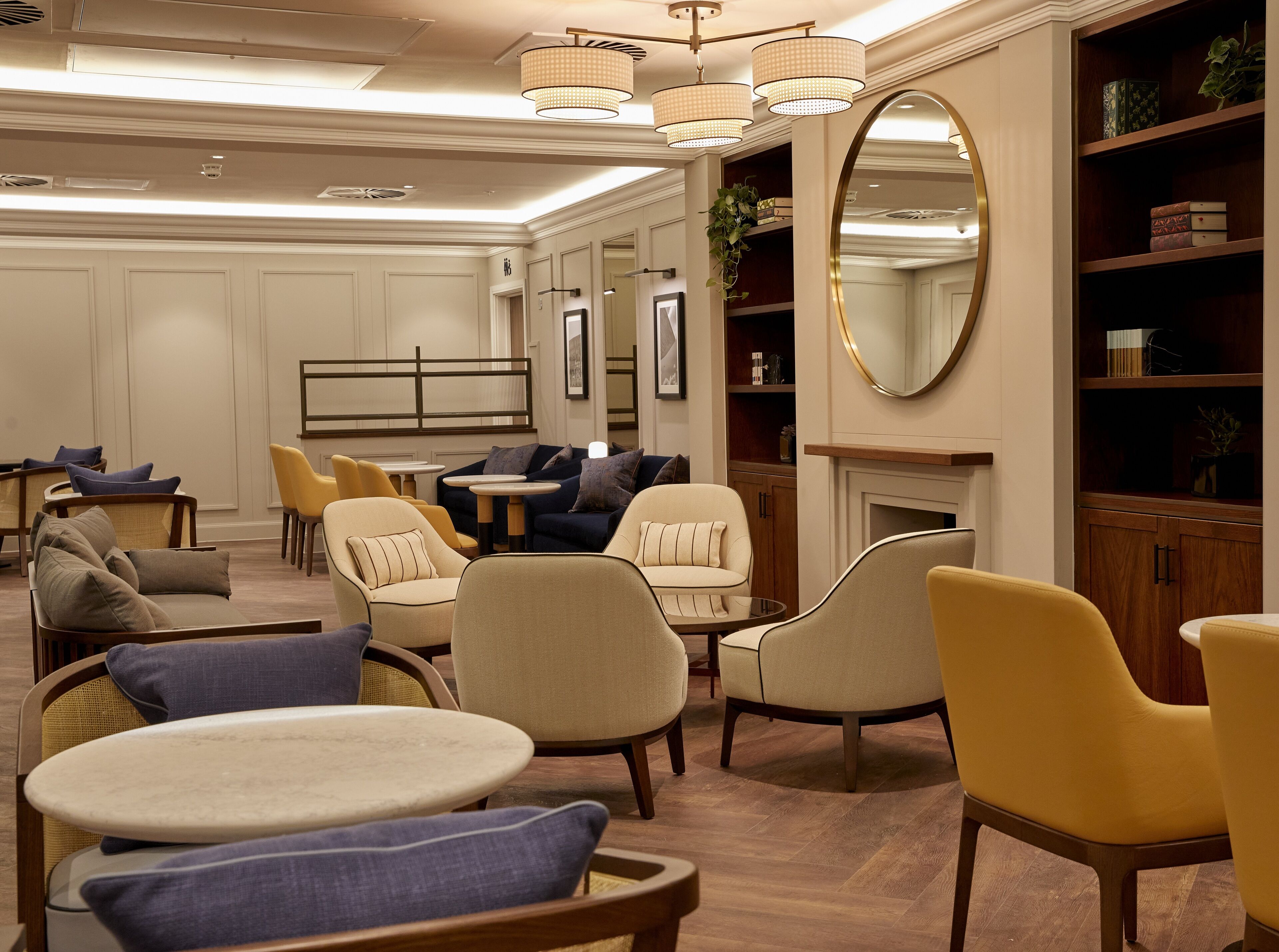 A well-lit lounge area with multiple seating options including sofas and chairs, a fireplace, and a bookshelf.