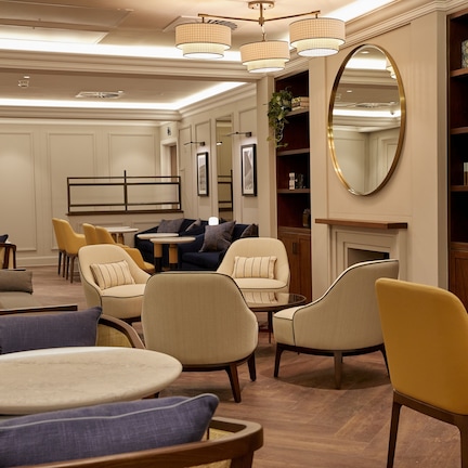 A well-lit lounge area with multiple seating options including sofas and chairs, a fireplace, and a bookshelf.