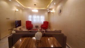 A living room with a wooden coffee table, two red armchairs, a grey sofa, and a television on a stand. - Nadi Paradise (Abuja)