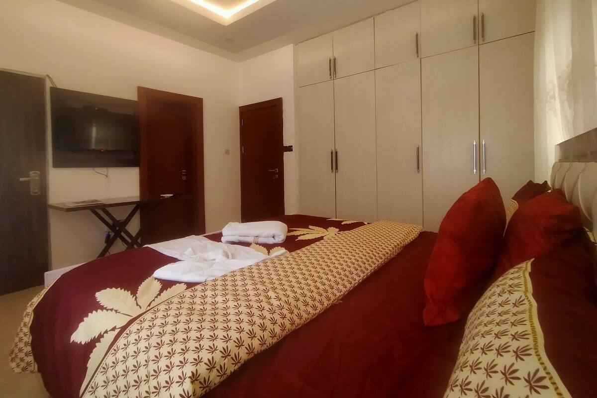 A hotel room with a bed, a TV mounted on the wall, a desk, and a wardrobe.