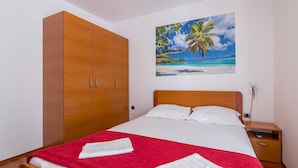 Una camera da letto con un letto, una coperta rossa, un armadio in legno, un comodino e un quadro raffigurante una spiaggia.