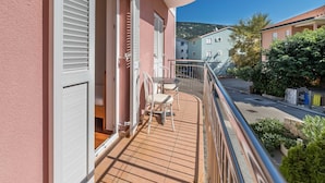 Un balcone con tavolo e sedie, vista sulla strada e un edificio con persiane.
