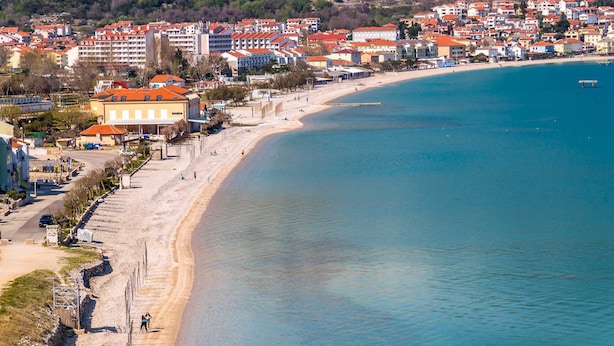 Una cittadina costiera con una spiaggia sabbiosa, edifici dai tetti rossi e un mare cristallino.