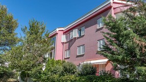 Un edificio a più piani con facciata rosa, persiane bianche e un balcone.