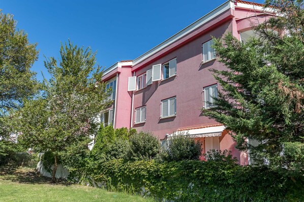 Un immeuble à plusieurs étages, doté d’une façade rose, de volets blancs et d’un balcon.