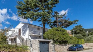 Un edificio blanco de dos pisos con un balcón, un muro de piedra y un coche estacionado.