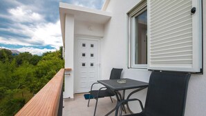 A balcony with a table and chairs, a white door, and a window with blinds. - Goran A2 - Cozy One-Bedroom Apartment with Parking Bliss for Two (Baška)