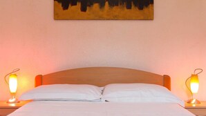 A neatly made bed with white linens, two bedside lamps, and a painting above the bed. - Goran A2 - Cozy One-Bedroom Apartment with Parking Bliss for Two (Baška)
