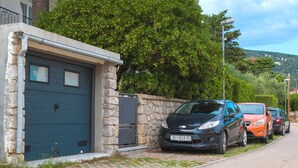 A residential street with a stone wall, a blue garage door, and parked cars. - Goran A2 - Cozy One-Bedroom Apartment with Parking Bliss for Two (Baška)