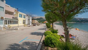 A coastal street with buildings, a sandy beach, and a clear view of the sea. - Dubravka, studio with sea view (Baška)