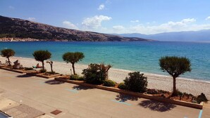 Une route côtière bordée d’arbres, avec des espaces de stationnement et donnant sur la plage.