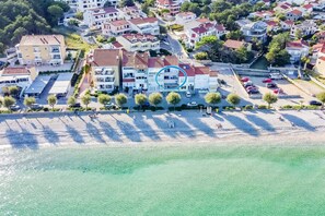 An aerial view of a coastal residential area with buildings, a beach, and a parking lot.