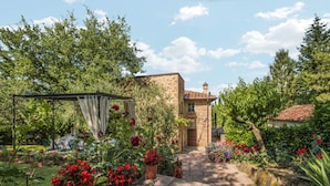 Een stenen gebouw met een tuin, een pergola met gordijnen en verschillende bloemen.